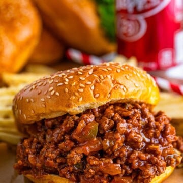 Saucy Dr Pepper sloppy joe piled high on a toasted sesame seed bun with waffle fries and a Dr Pepper can in the background.