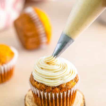 Cinnamon Cream Cheese Frosting being piped in a tall swirl onto a cupcake.