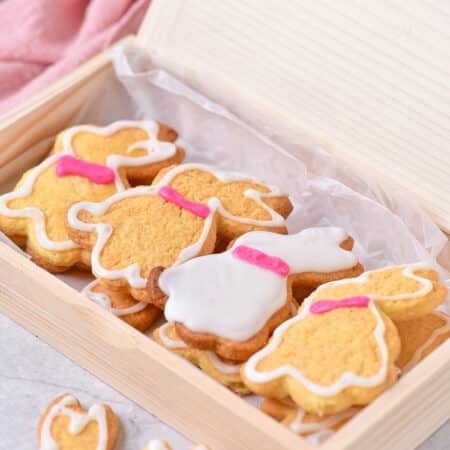 Decorated Easter bunny cookies with white glaze outlines and pink collars arranged in a wooden gift box.