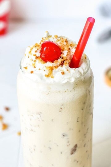 A tall Chick Fil A caramel milkshake topped with whipped cream, blondie crumbles, and a cherry.