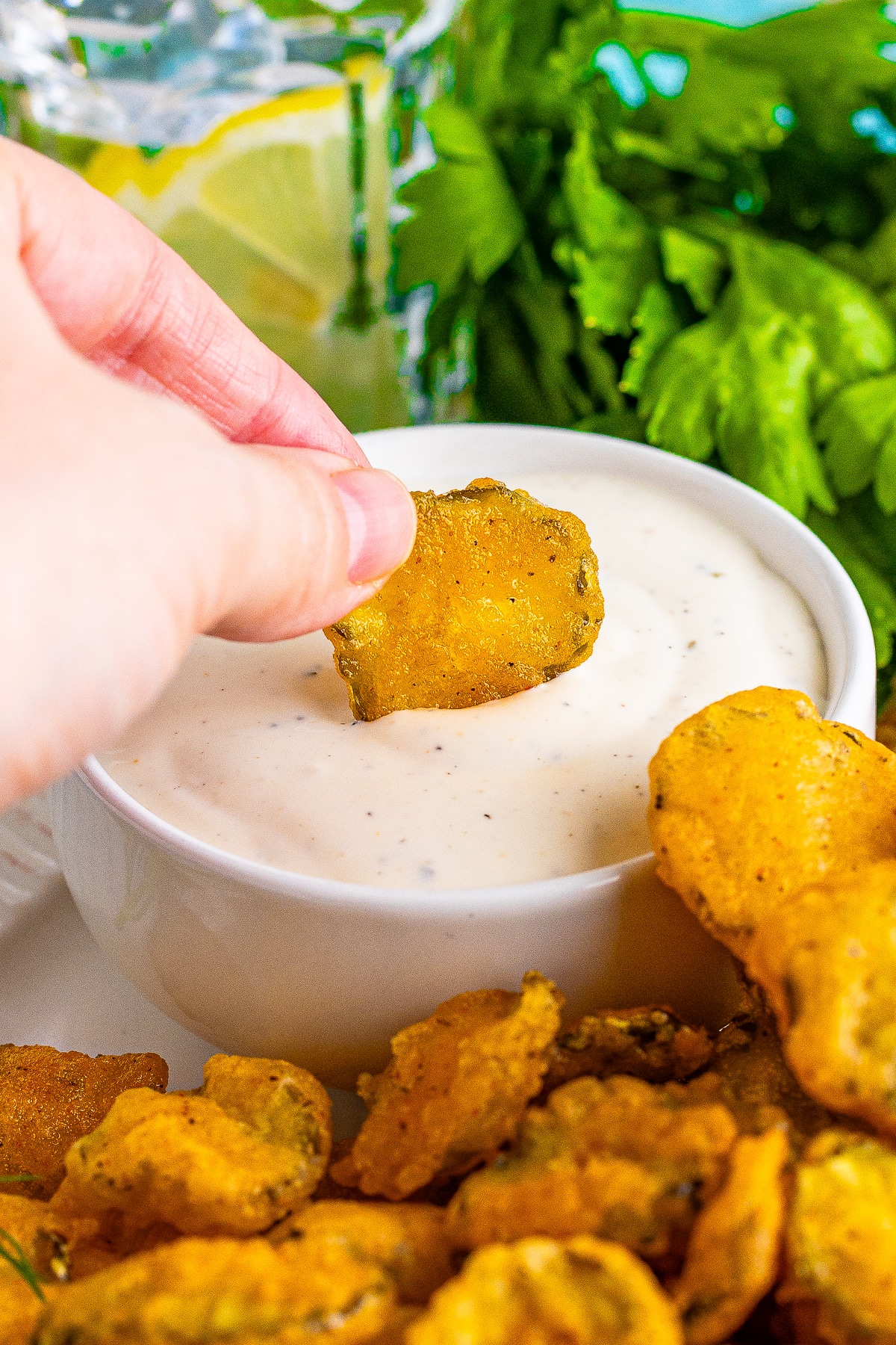 a hand dipping deep fried pickles recipe into ranch