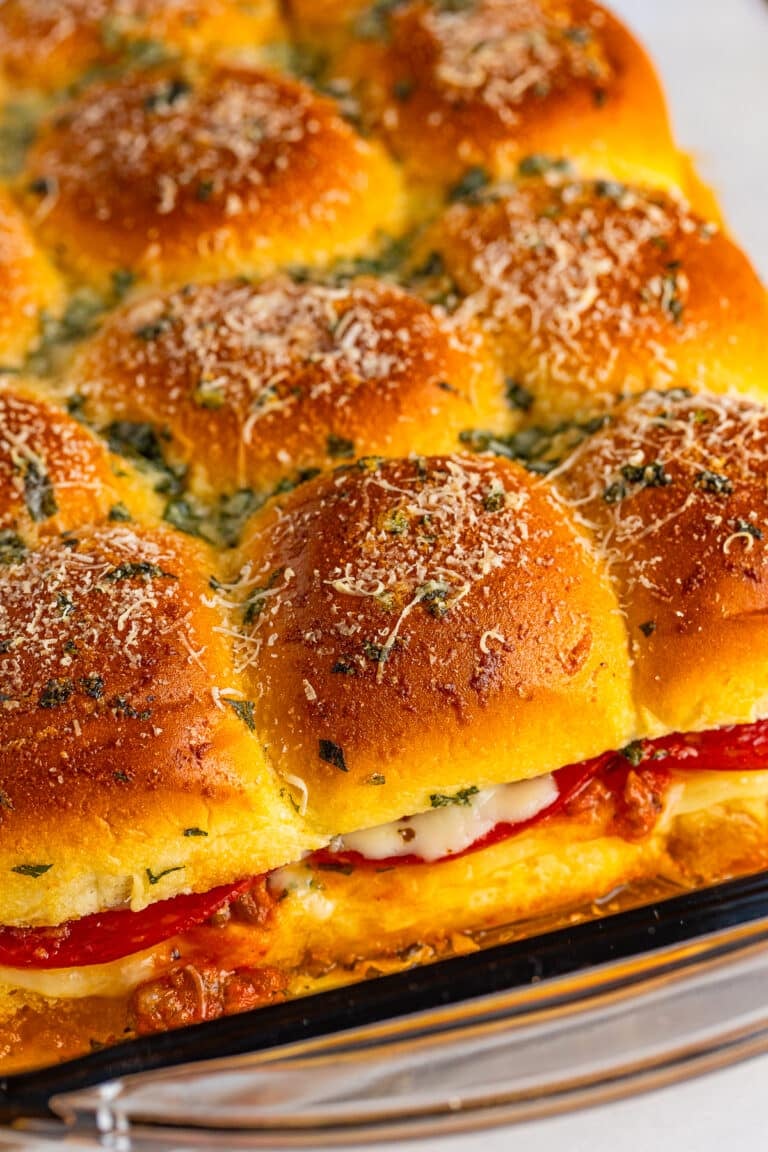 A pan of golden baked pizza sliders topped with parmesan and basil.