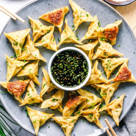 A plate of pan fried pork dumplings with crispy bottoms and a soy dipping sauce.