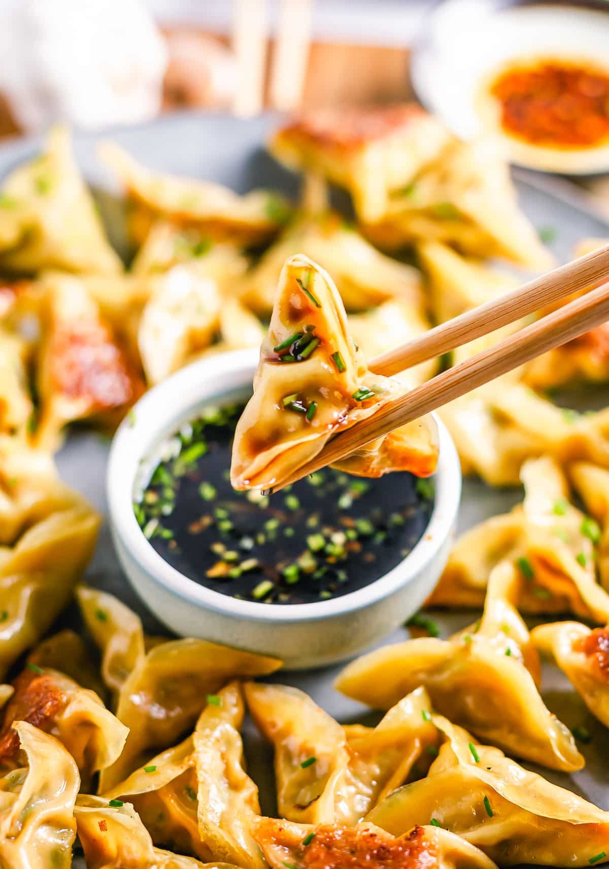 chopsticks holding up pork and chive dumplings that have been dipped in sauce in air