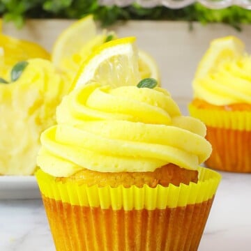 A lemon cheesecake cupcake topped with a swirl of yellow frosting and a lemon slice.