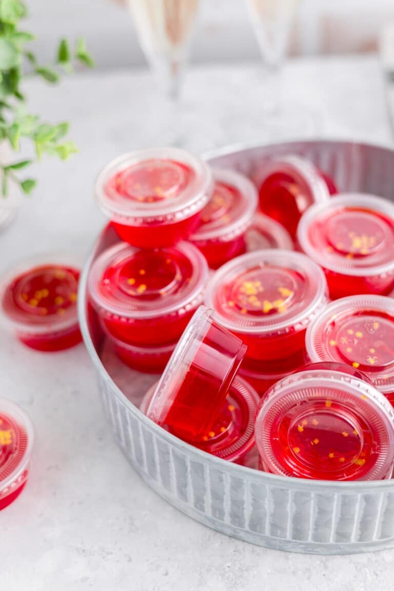 Non alcoholic jello shots in plastic cups topped with sprinkles on a tray.