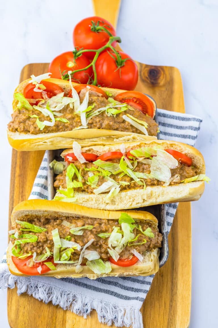 Three slow cooker chopped cheese sandwiches on a wooden board topped with lettuce and tomato.