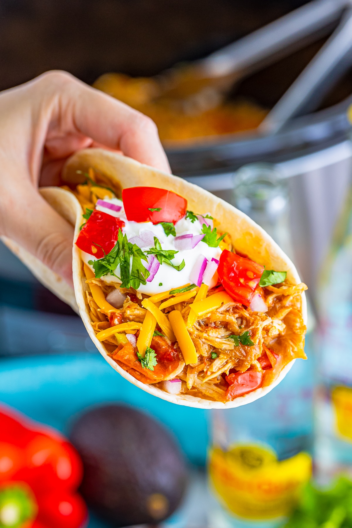 a hand holding up slow cooker mexican shredded chicken tacos in air