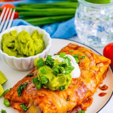 Easy smothered beef burritos plated with guacamole, sour cream, and green onion.