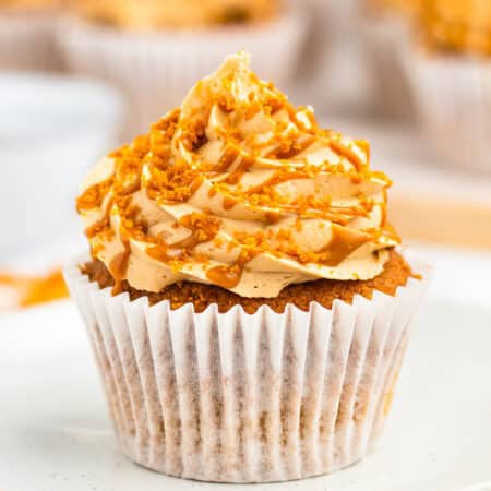 Biscoff cupcake with a tall cookie butter frosting swirl and Speculoos cookie crumbs on a white plate.