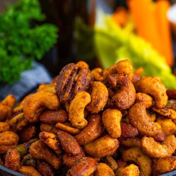 A bowl of buffalo ranch roasted nuts served with celery and a cold drink.