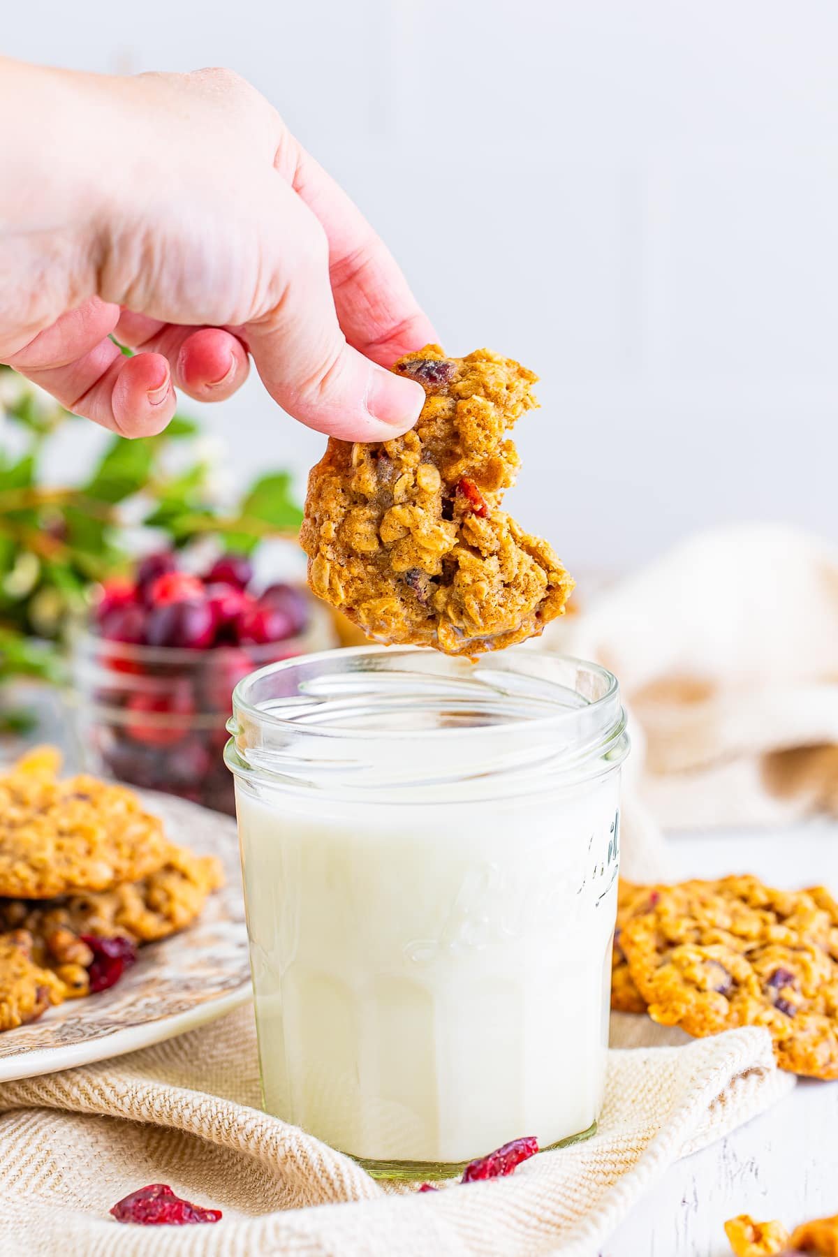 a hand dipping Cranberry Oatmeal Cookies in a glass of milk