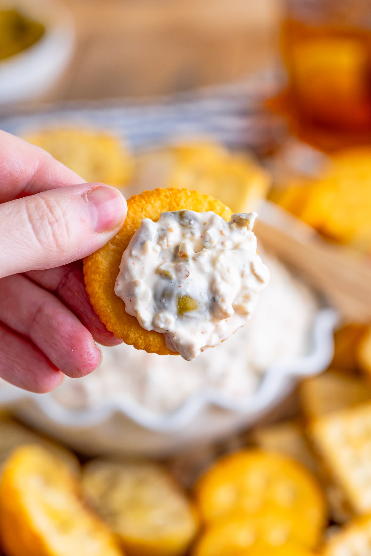 a hand holding up a cracker with olive dip on it in air