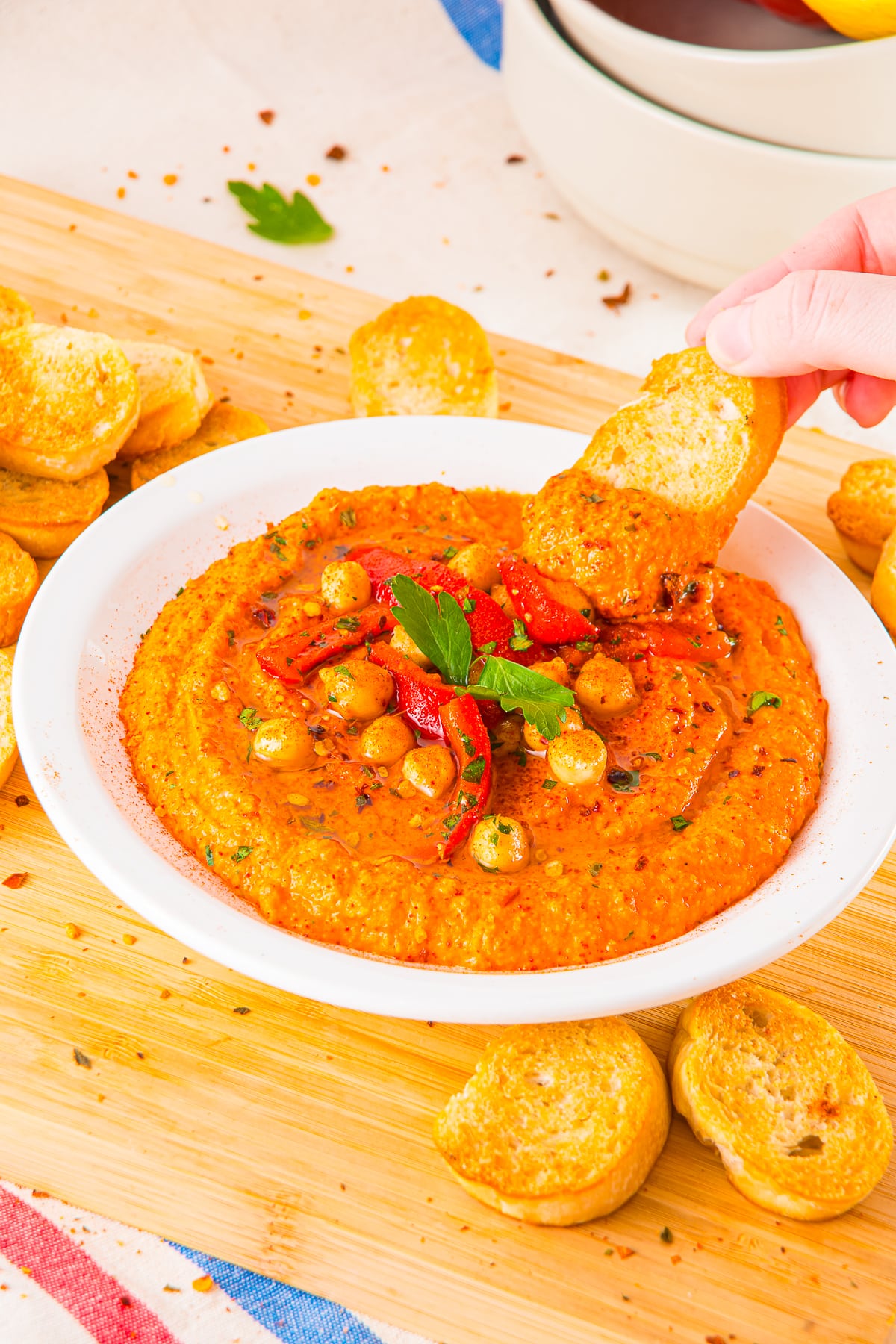 a hand dipping crostini into Red Pepper Hummus