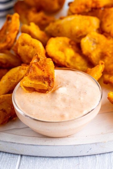 A bowl of creamy Copycat Outback Bloomin Onion Sauce with a fried onion petal being dipped in.