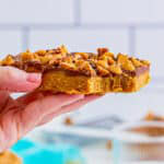 A stack of no-bake peanut butter bars with a chocolate layer and toffee and pecan topping.
