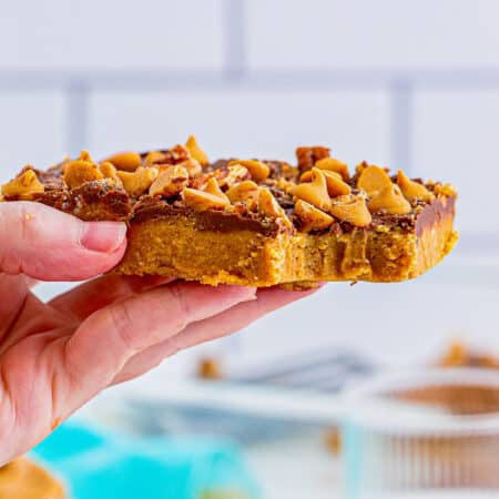 A stack of no-bake peanut butter bars with a chocolate layer and toffee and pecan topping.