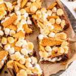 Smores brownies with toasted marshmallows and graham cracker pieces cut into squares on parchment.