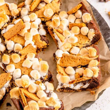 Smores brownies with toasted marshmallows and graham cracker pieces cut into squares on parchment.