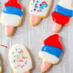 Popsicle shaped cut out sugar cookies decorated with red, white, and blue icing on parchment.