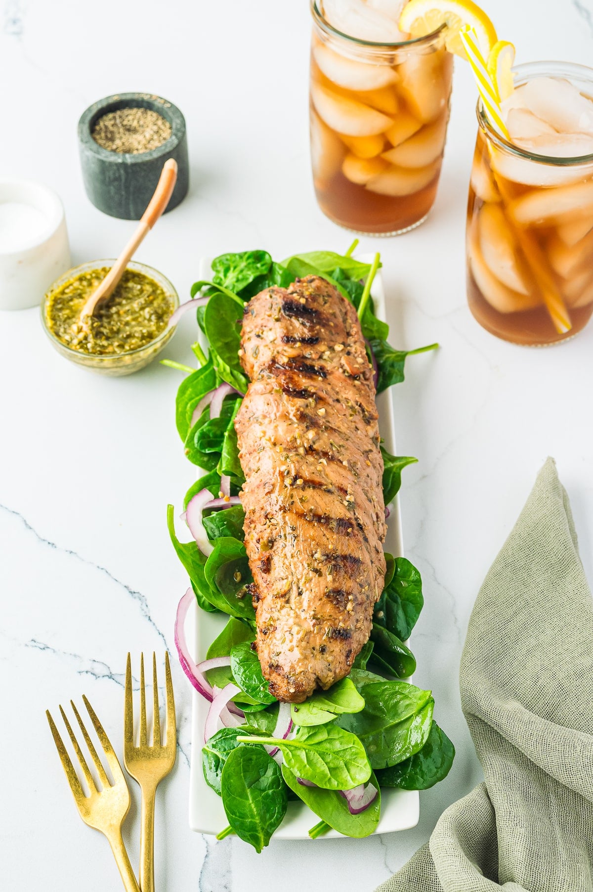 Pesto Marinated Grilled Pork Tenderloin, tender pork tenderloin, marinated in a flavorful pesto sauce and grilled. Ready in about 30 minutes! Recipe from ThisSillyGirlsKitchen.com Marinated Pork Tenderloin on a serving platter with spinach