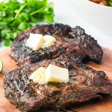 Grilled cilantro lime ribeye steaks topped with herb butter on a wooden board.