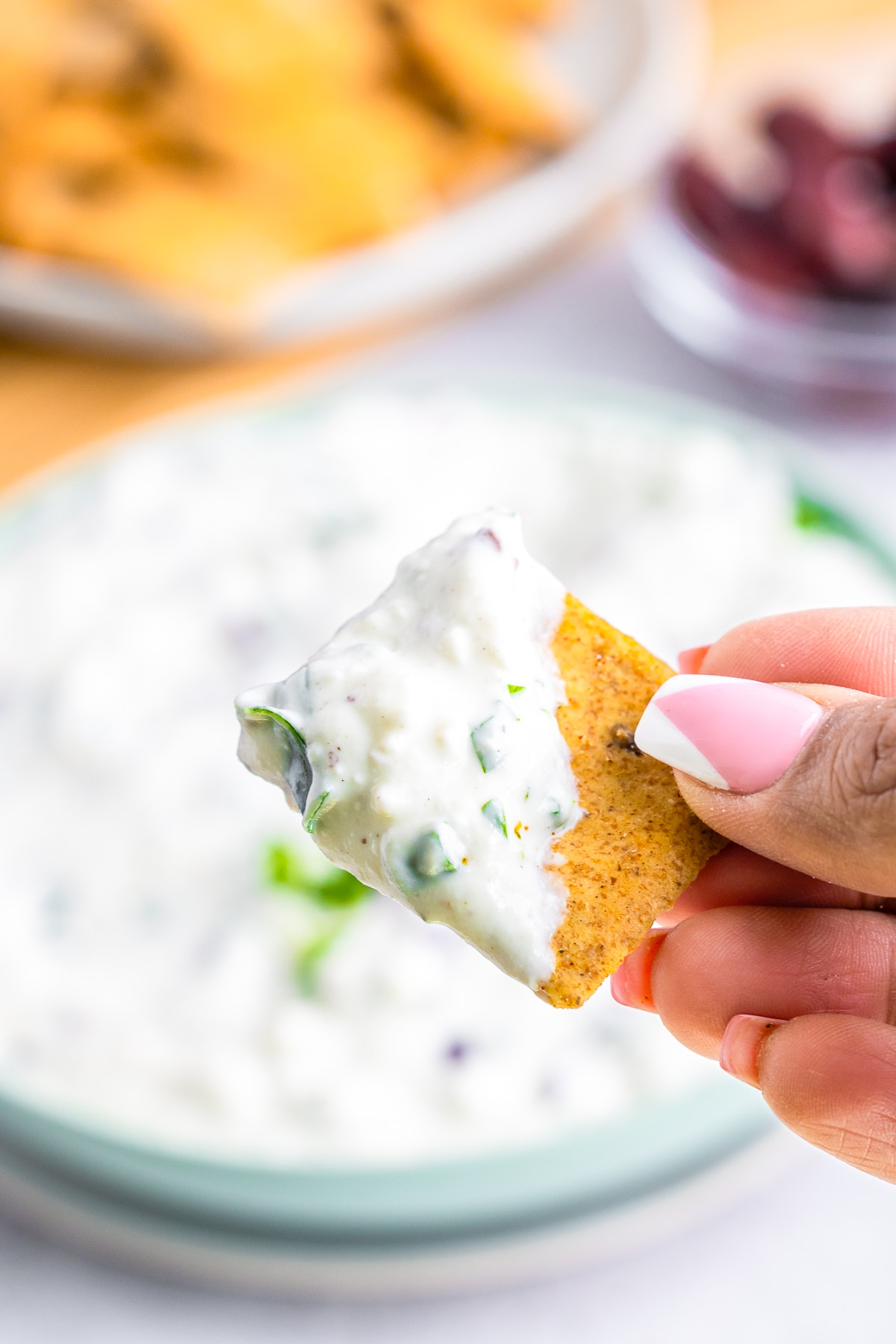 a hand holding up a cracker with Greek Yogurt Dip on it in air