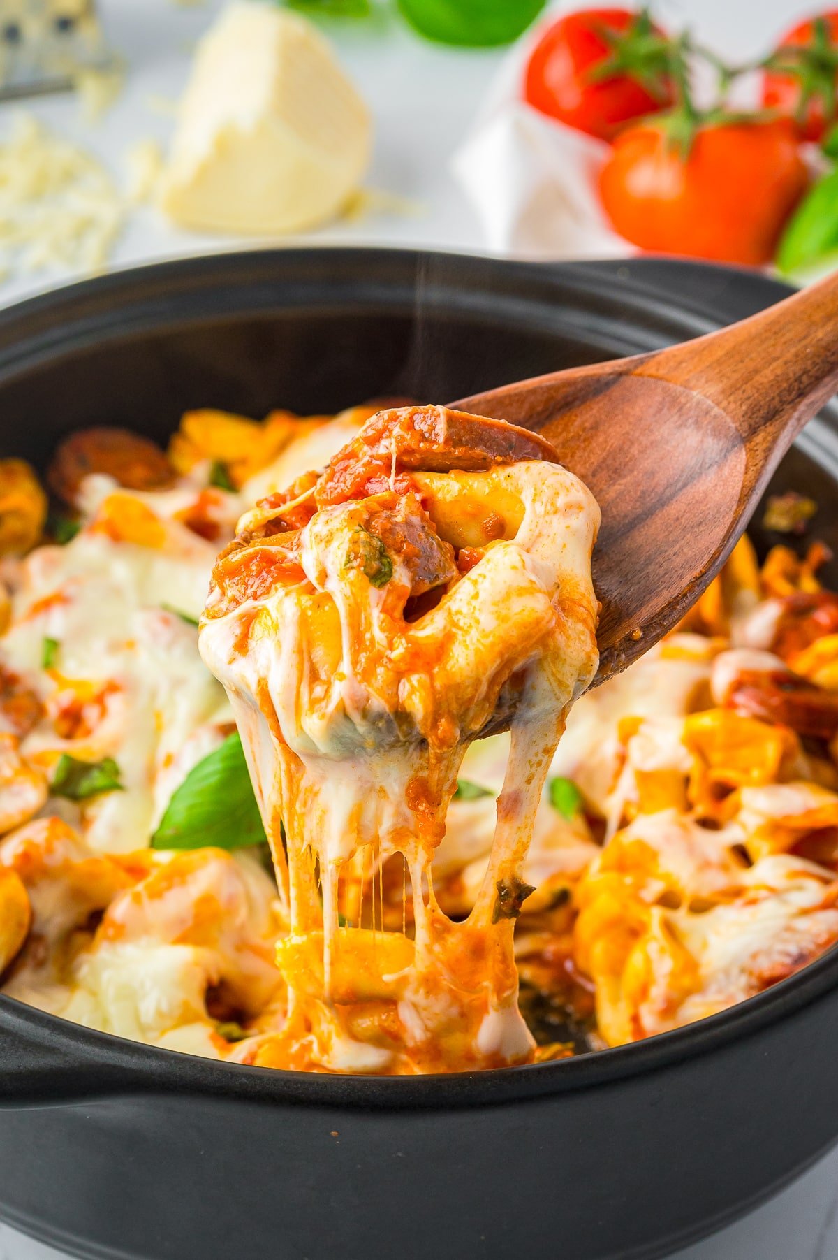 a wooden spoon lifting a bite of Baked Tortellini out of the baking dish