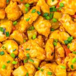 A bowl of sweet chili chicken with pineapple and bell pepper served over white rice and garnished with scallions.