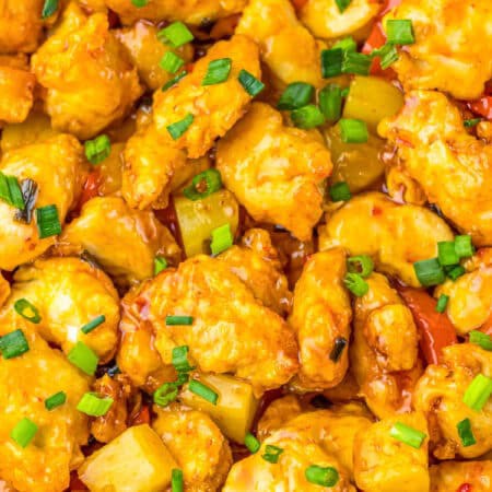 A bowl of sweet chili chicken with pineapple and bell pepper served over white rice and garnished with scallions.