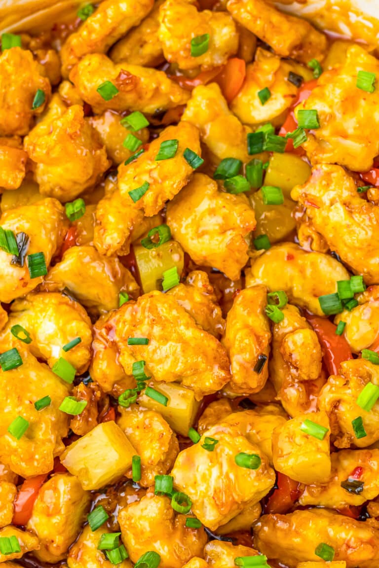 A bowl of sweet chili chicken with pineapple and bell pepper served over white rice and garnished with scallions.