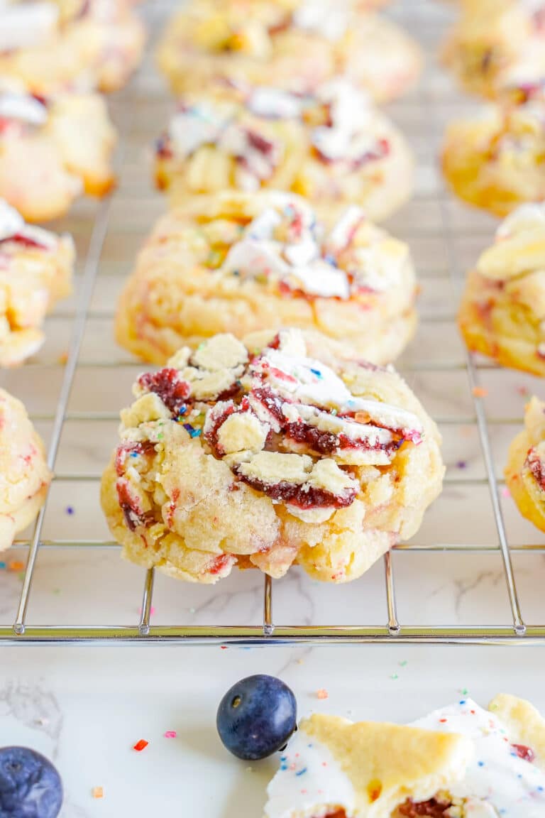 Blueberry pop tart sugar cookies on a wire rack topped with crushed Pop-Tarts and sprinkles.