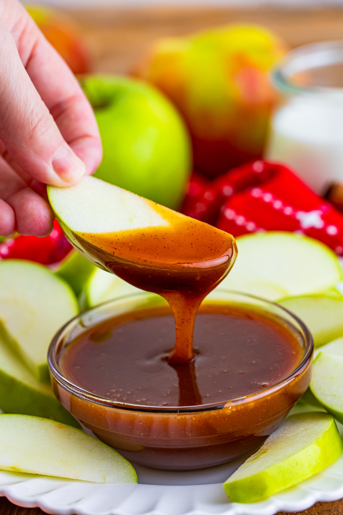 a hand holding up an apple sliced that was dipped into Easy Caramel Sauce in air