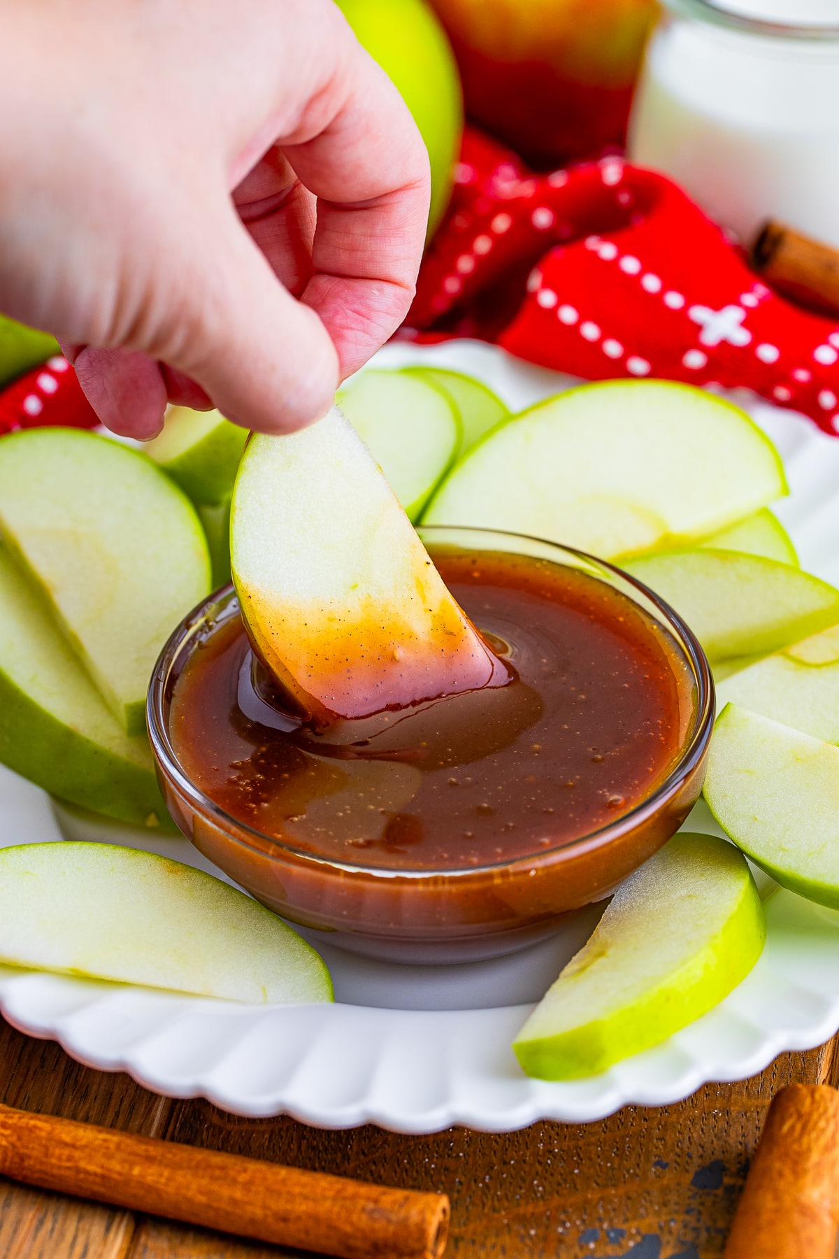 a hand dipping an apple slice into Easy Caramel Sauce