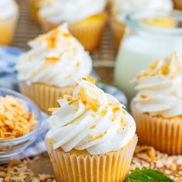 A Coconut Cupcake with tall swirled coconut frosting and toasted coconut in front of a jar of milk.