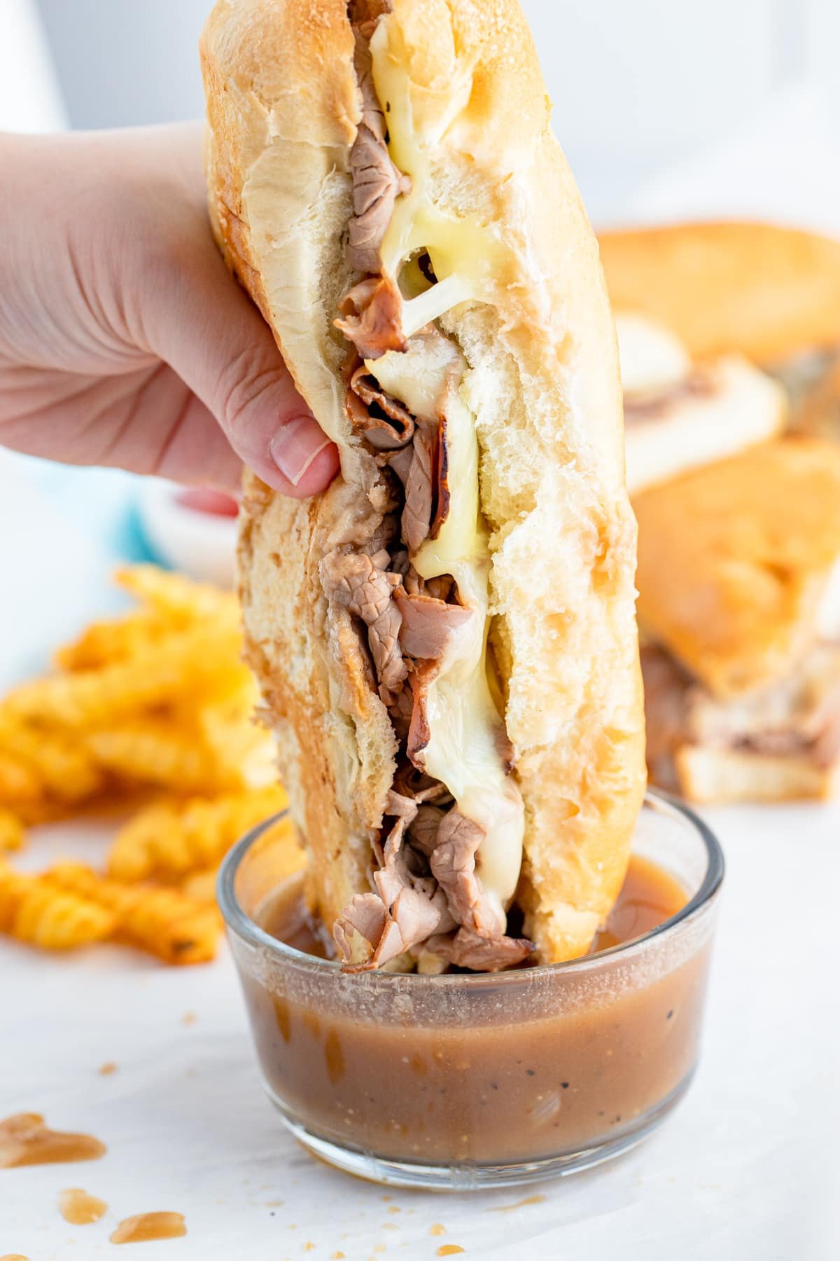 a hand dipping french dipped sandwich recipe into au jus