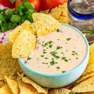A bowl of creamy queso dip with a tortilla chip scooping it up, garnished with diced tomatoes.
