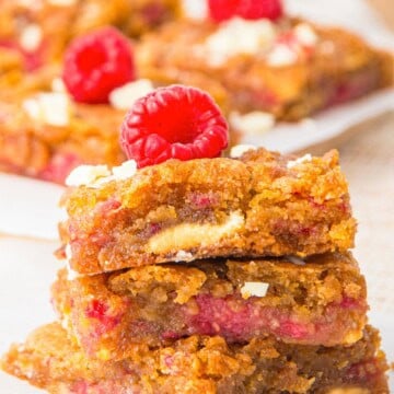 A stack of raspberry brownies studded with white chocolate and topped with a fresh raspberry.
