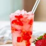 Strawberry Acai Refresher in a glass with crushed ice, fresh strawberries, and a straw.