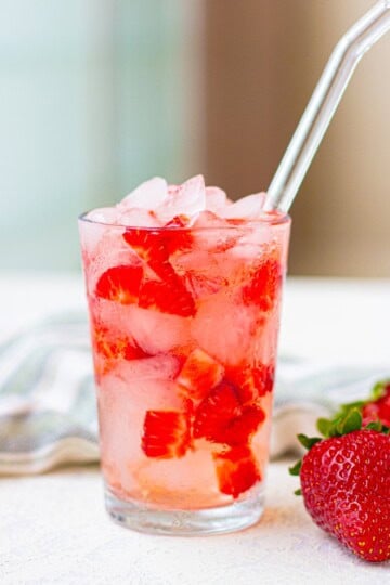 Strawberry Acai Refresher in a glass with crushed ice, fresh strawberries, and a straw.