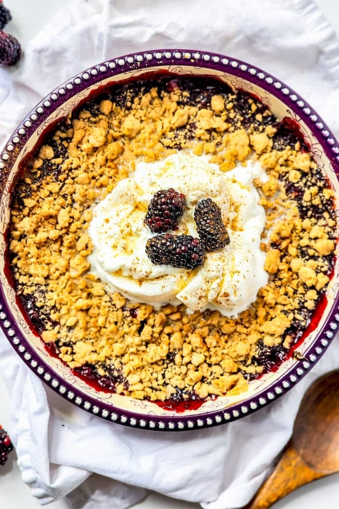 A baking dish of blackberry crisp topped with a scoop of whipped cream.