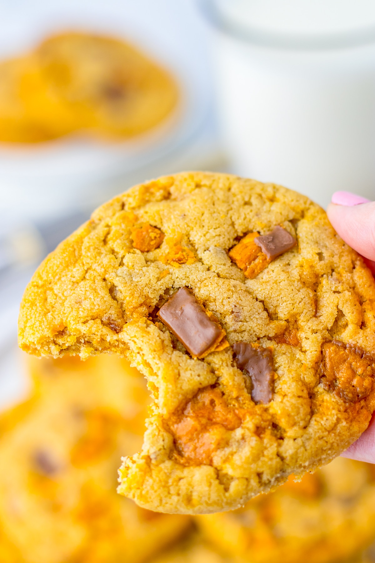 a hand holding up Butterfinger Cookies with a bite taken out in air