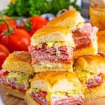 A stack of Italian sliders showing layers of meats, cheese, and lettuce on Hawaiian rolls.