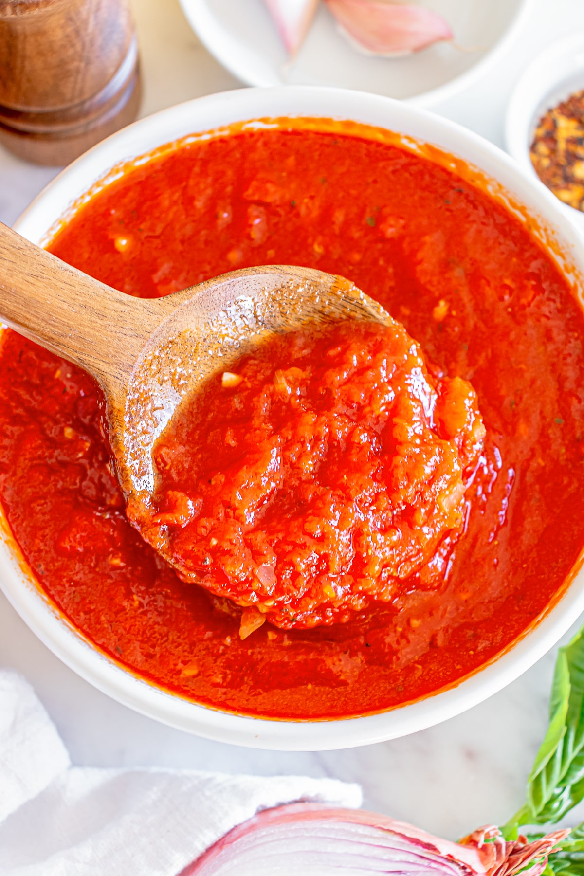 overhead image of homemade marinara sauce in a white bowl with a wooden spoon