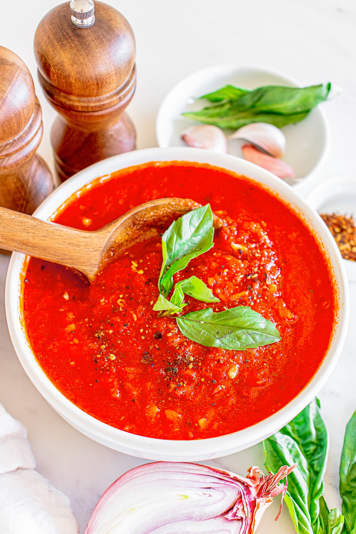 overhead image homemade marinara sauce in a white bowl with basil garnish