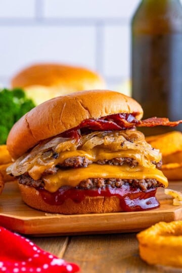 A BBQ bacon smash burger stacked tall with cheddar and onions on a bun.