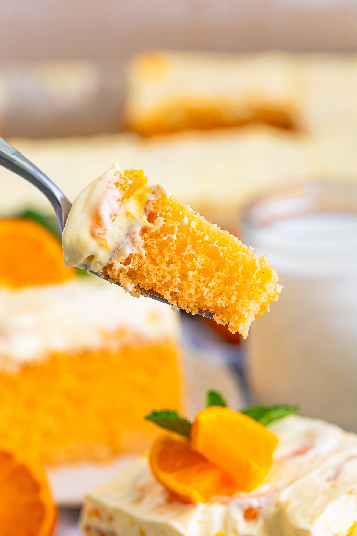 a hand holding up a bite of Orange Creamsicle Cake on a fork in air