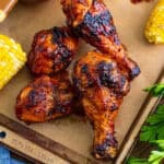 Grilled BBQ chicken legs on a wooden board with grilled corn.