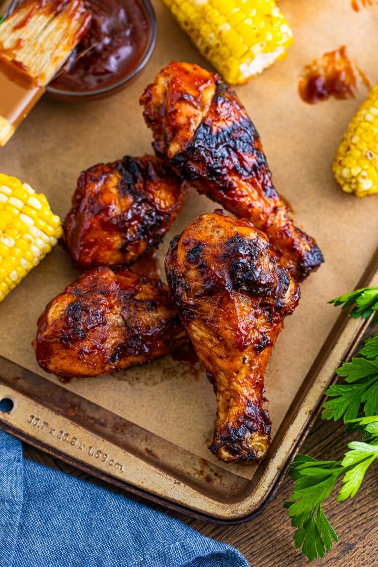 Grilled BBQ chicken legs on a wooden board with grilled corn.