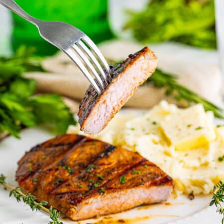 A grilled balsamic marinated pork chop sliced to show the juicy interior, served with mashed potatoes.